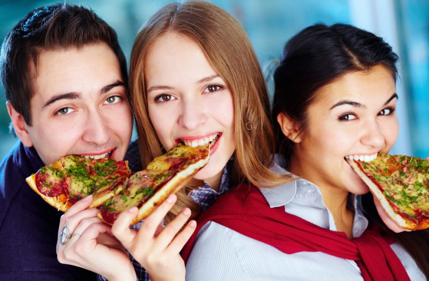 Image of happy teenage friends eating pizza and looking at camera